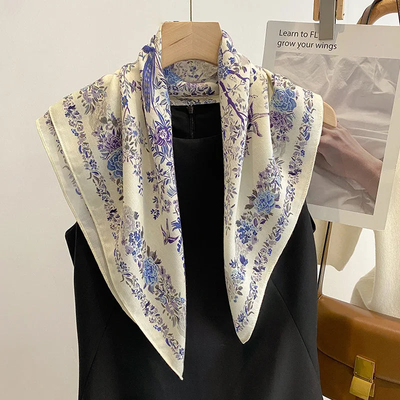 Foulard carré en satin, imprimé bleu cobalt avec oiseaux et fleurs délicates, suspendu élégamment.